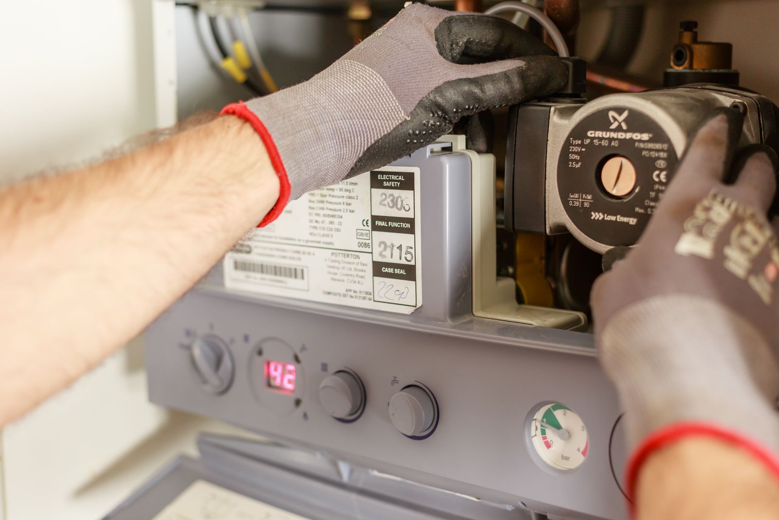Gloved hands servicing the controls and circulator on a heating unit