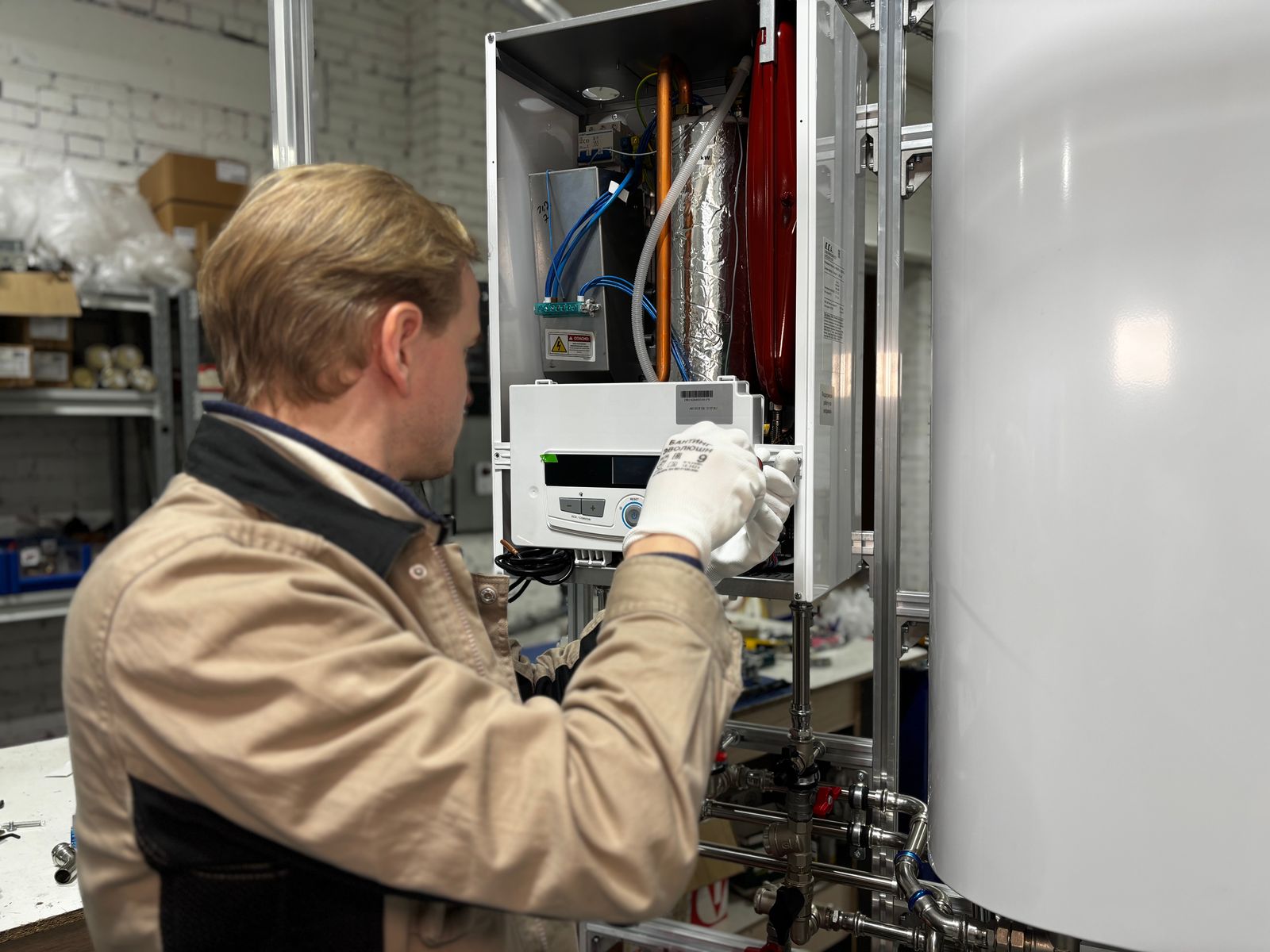 A technician services a wall-hung heating unit beside a hot water tank, the kind of swap common in Innisfil lakefront homes