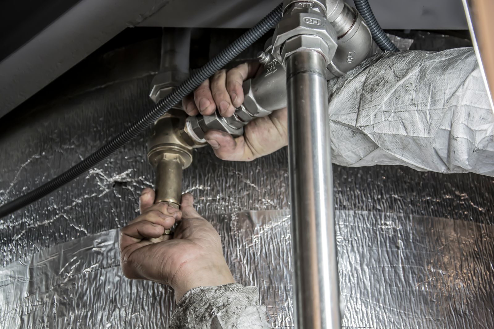 Hands fitting new supply lines under a fixture, typical rough-in work in Angus new builds