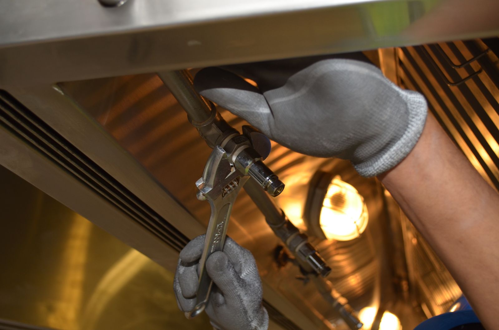 A plumber's gloved hands tighten a fitting with an adjustable wrench under a sink
